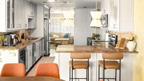 A modern kitchen with white cabinets, a marble countertop, and a central island with bar stools. - Family Resort: Pool & Outdoor Theater near Old Town, Golf, Baseball, and Events (Scottsdale)