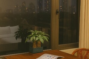 A room with a wooden table, a potted plant, and a window with a city view. - MingFang Hotel (Bac Ninh)