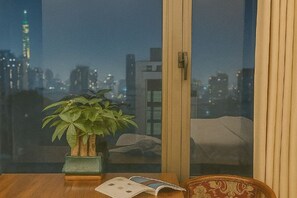 A room with a view of a city skyline, a wooden table with a book, and a potted plant. - MingFang Hotel (Bac Ninh)