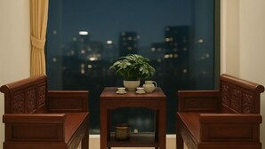 A room with a view of a cityscape at night, a small table with a potted plant, and two wooden chairs. - MingFang Hotel (Bac Ninh)
