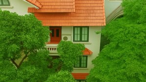 A multi-story building with a red-tiled roof and green shutters, surrounded by lush green trees. - MingFang Hotel (Bac Ninh)