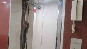 An elevator with a glass door, a red wall, and a phone mounted on the wall. - MingFang Hotel (Bac Ninh)