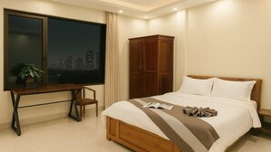 A bedroom with a bed, a desk, a chair, a wardrobe, and a window with a city view. - MingFang Hotel (Bac Ninh)