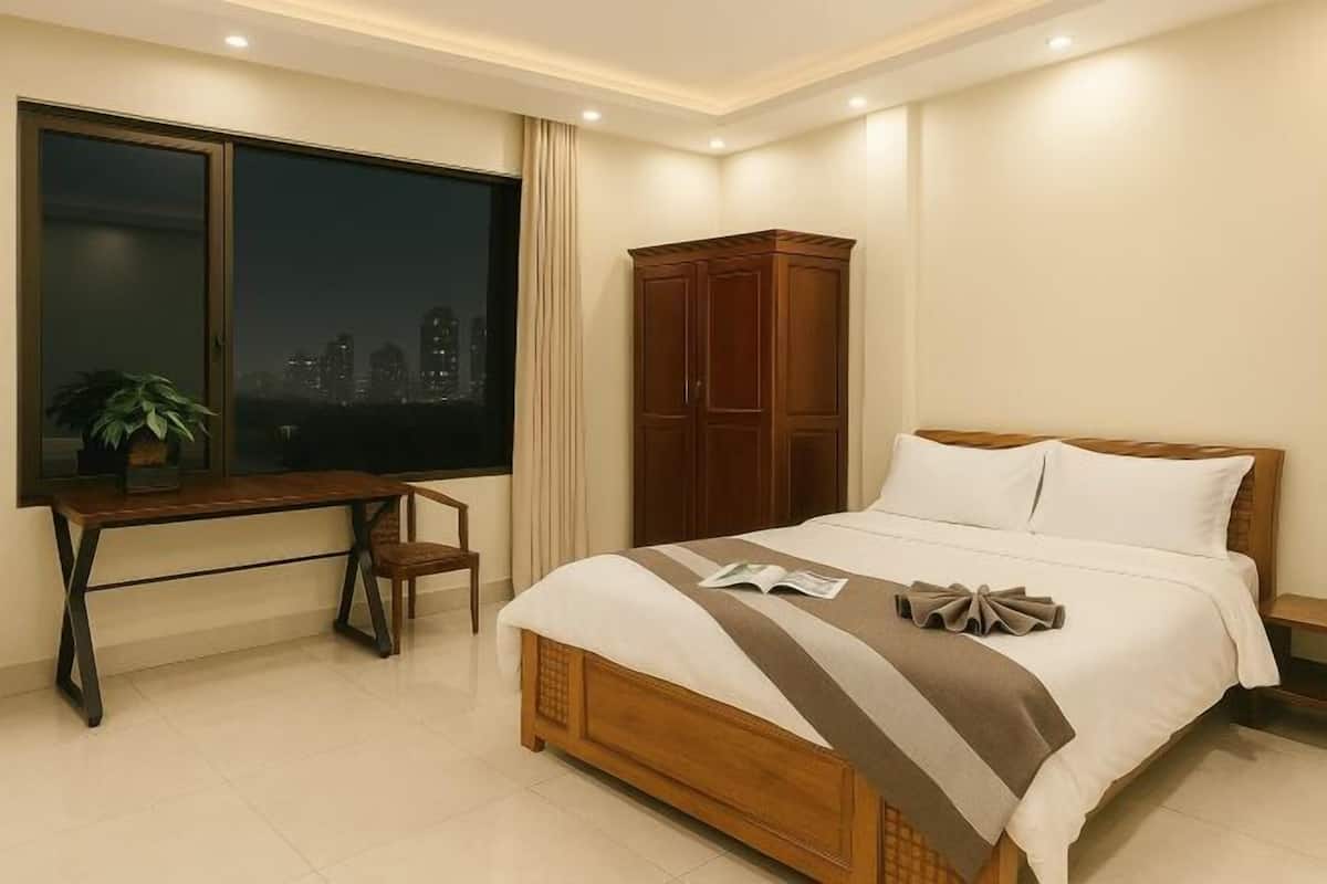 A bedroom with a bed, a desk, a chair, a wardrobe, and a window with a city view.