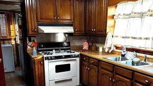 Una cocina con armarios de madera, estufa, lavaplatos y una ventana con cortinas.