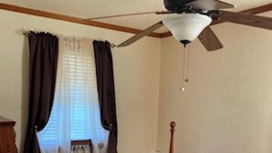 Un dormitorio con cama, ventilador de techo y ventana con cortinas.