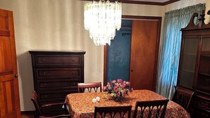 Comedor con candelabro, sillas de madera, mesa con mantel floral, alfombra con motivos florales y aparador de madera.