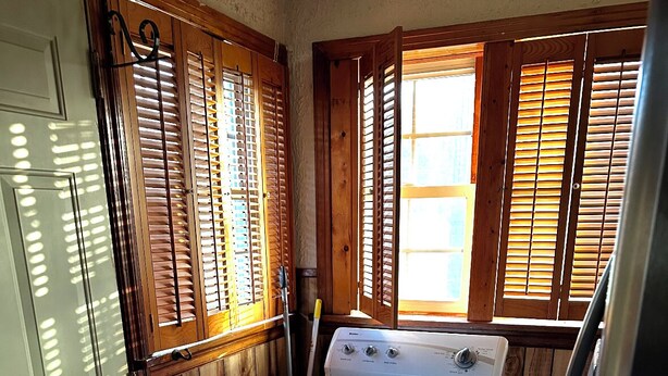 Un lavadero con lavadora y secadora, contraventanas de madera y suelo de hormigón.