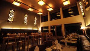 Un ristorante con soffitto e pareti in legno, ampie finestre e tavoli apparecchiati con tovaglie e tovaglioli bianchi.