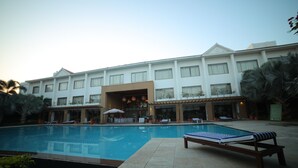Un hotel con piscina, lettini e una zona coperta con ombrelloni.