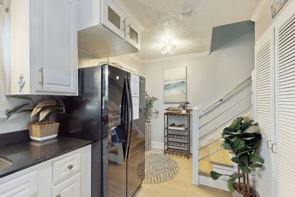 Una cocina moderna con armarios blancos, un refrigerador negro y una escalera que sube a otro nivel.