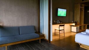 Une pièce avec un plancher en bois, un canapé bleu, un bureau avec une chaise, un téléviseur fixé au mur et un lit.
