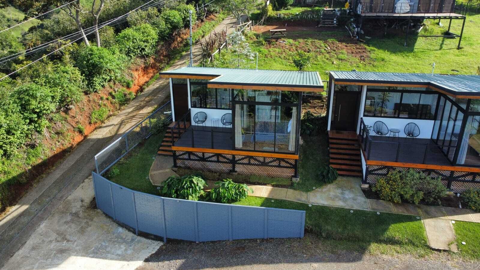A modern house with two glass-enclosed rooms, a deck, and a fenced garden.