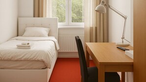 A hotel room with a bed, a desk with a chair, a lamp, and a window with curtains. - King Hotel (Huddinge)