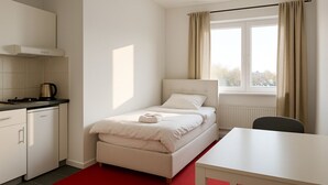 A compact hotel room with a bed, a small table, a kitchenette, and a window with curtains. - King Hotel (Huddinge)