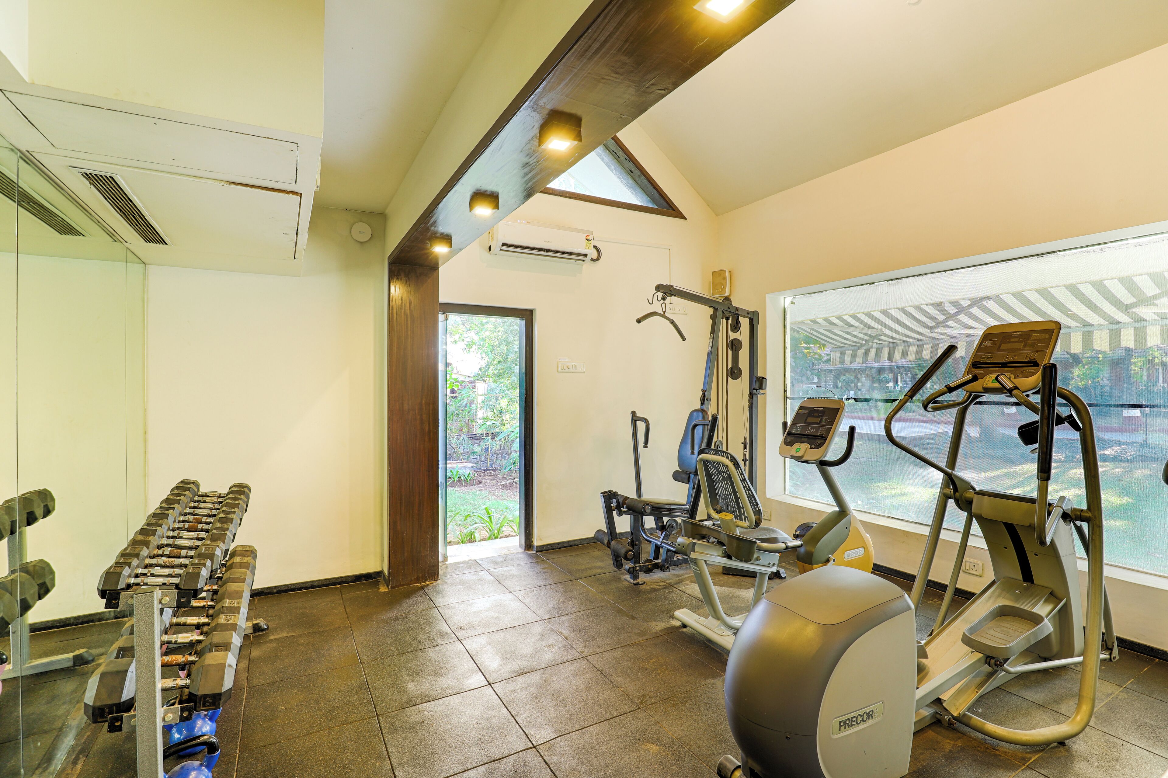 Un gimnasio con equipo de ejercicio, un ventanal y vistas a zonas verdes.