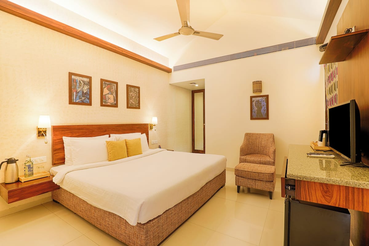 A hotel room with a large bed, a chair, a television, and a small refrigerator.