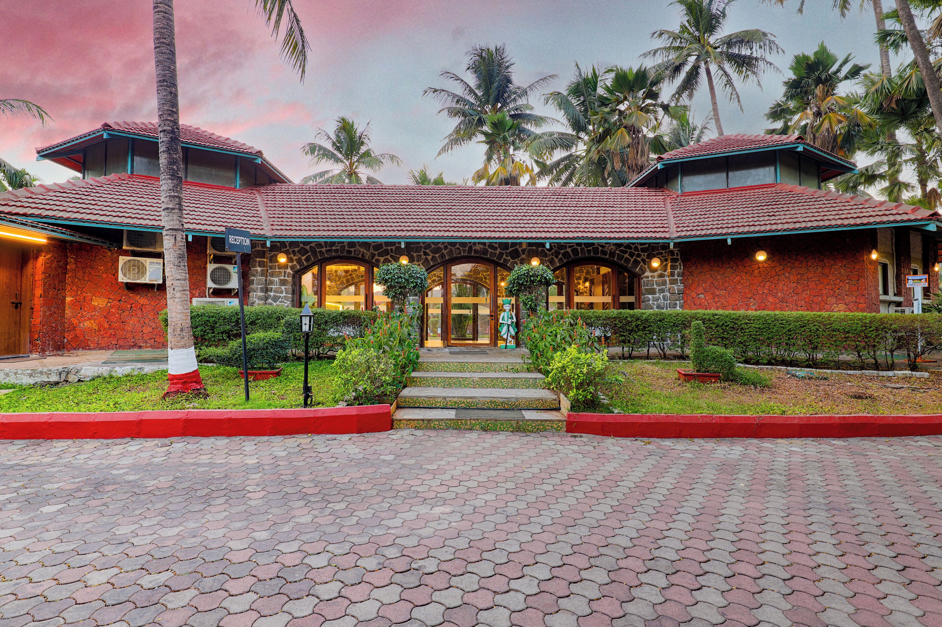 Un hotel con techo de tejas rojas, fachada de piedra y un jardín bien cuidado con palmeras y arbustos.