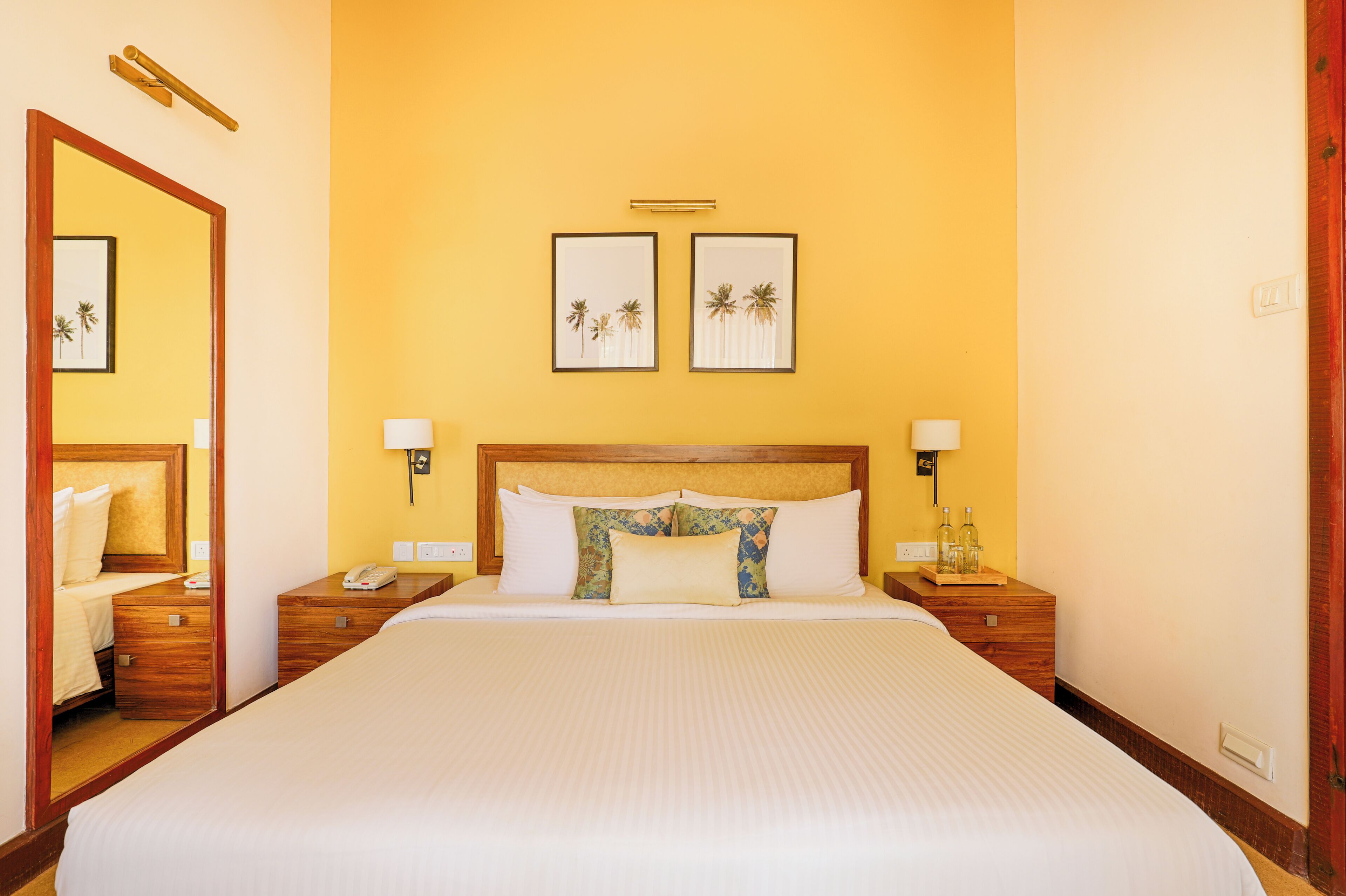 Habitación de hotel con una cama grande, cabecera de madera, dos mesitas de noche con lámparas y cuadros en la pared.