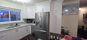 Cozinha moderna com armários brancos, eletrodomésticos de aço inoxidável e janela com vista para casas.