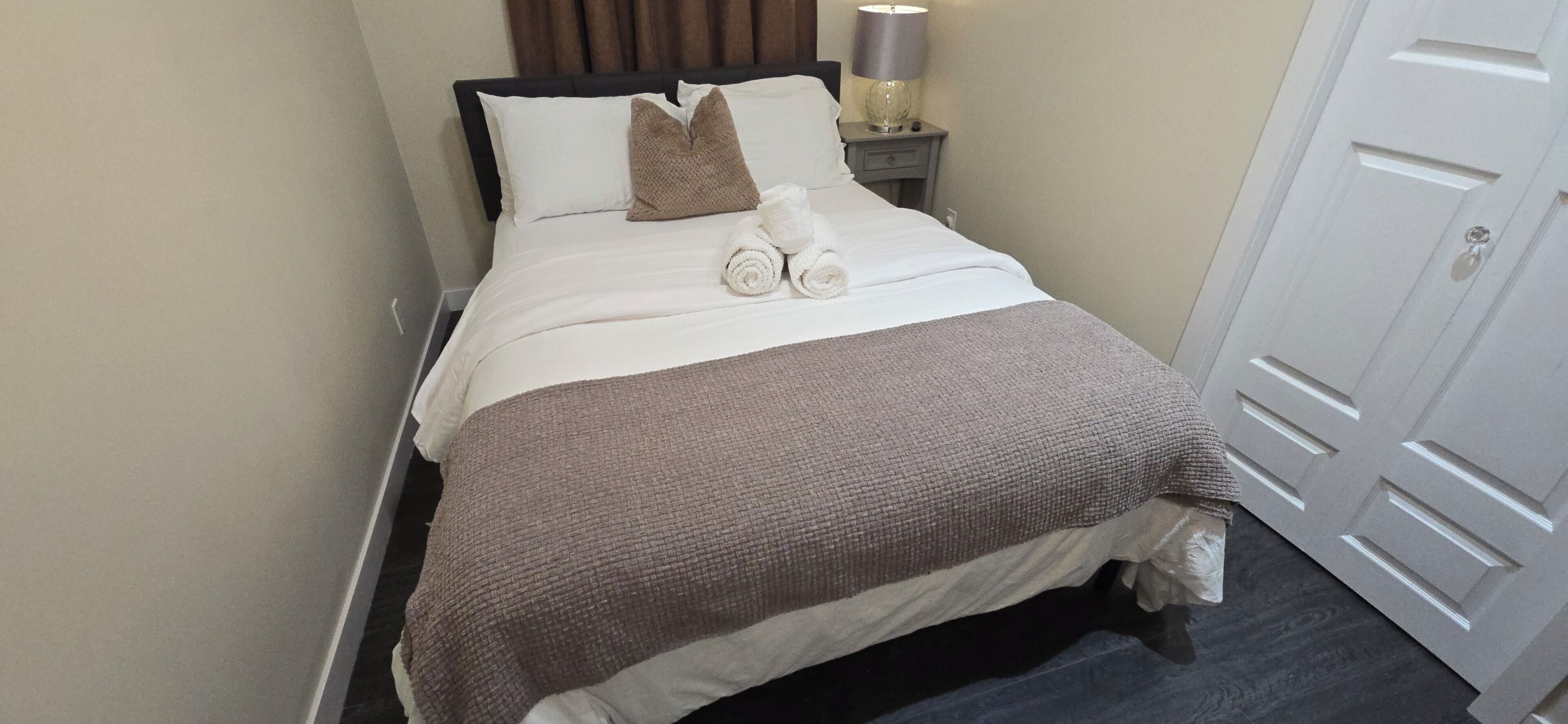 A neatly made bed with a brown blanket, white pillows, and rolled towels.