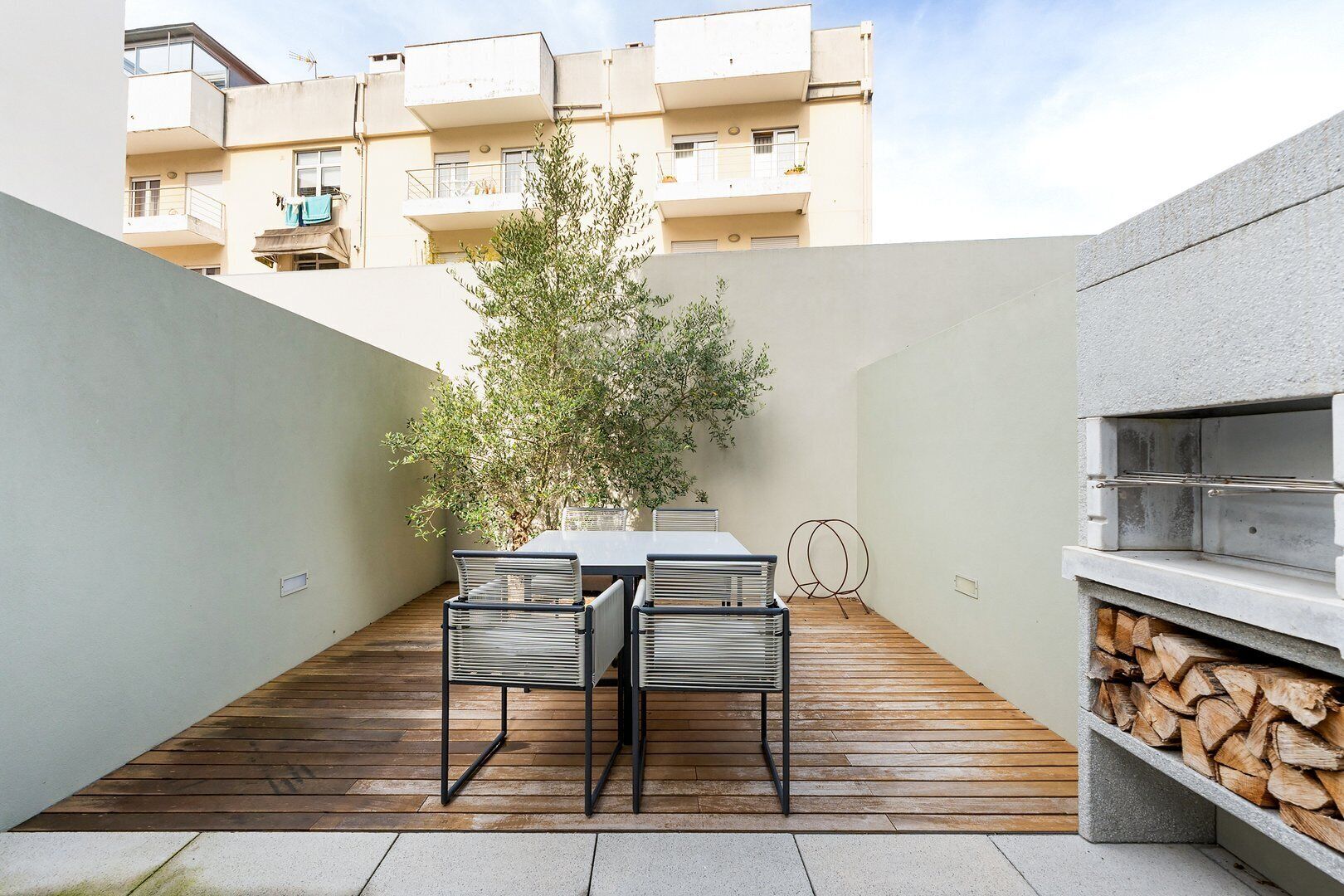 A patio with a table and chairs, a grill, and a tree.