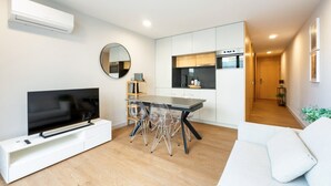 Ein modernes Wohnzimmer mit Flachbildfernseher, einem Esstisch mit Stühlen, einem weißen Sofa und einer Küchenzeile mit Schränken und einer Mikrowelle.
