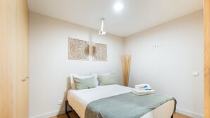 Ein Schlafzimmer mit einem Bett, einem Nachttisch mit Lampe und einem Fenster mit Vorhängen.