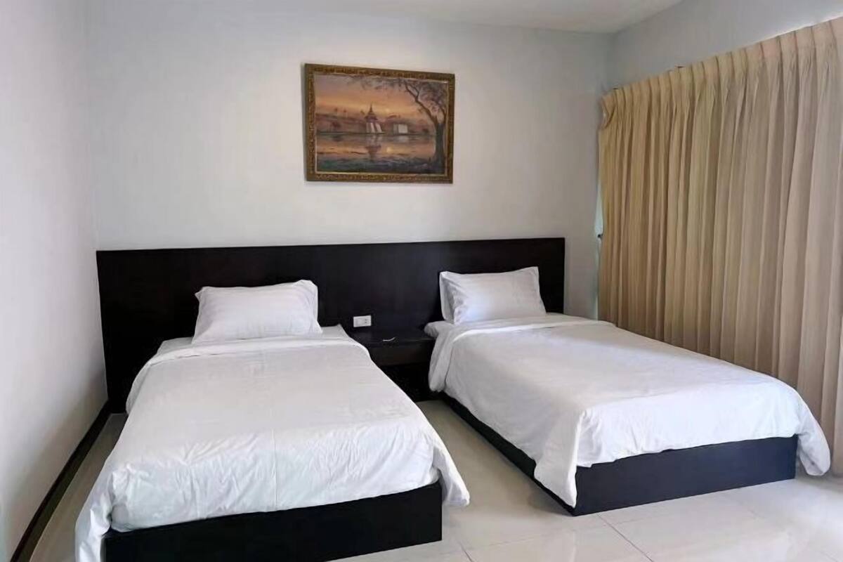 A hotel room with two single beds, a painting on the wall, and a large window with curtains.