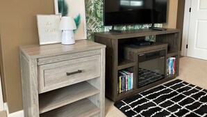 A wooden entertainment unit with a flat-screen TV, a lamp, and a framed quote.