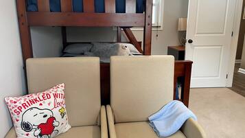 Een stapelbed met hoofdeinde, twee beige fauteuils, een kussen met Snoopy-print en een blauwe handdoek.