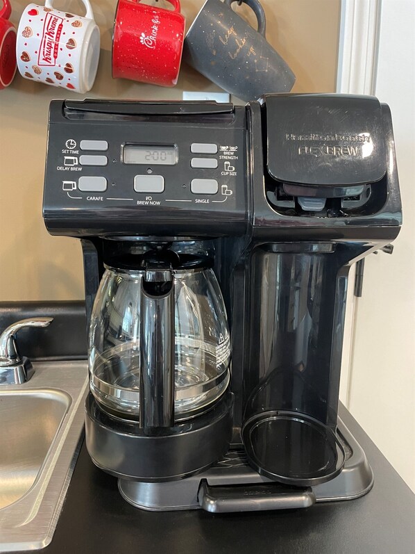 A coffee maker with a digital display, a carafe, and a single cup holder.