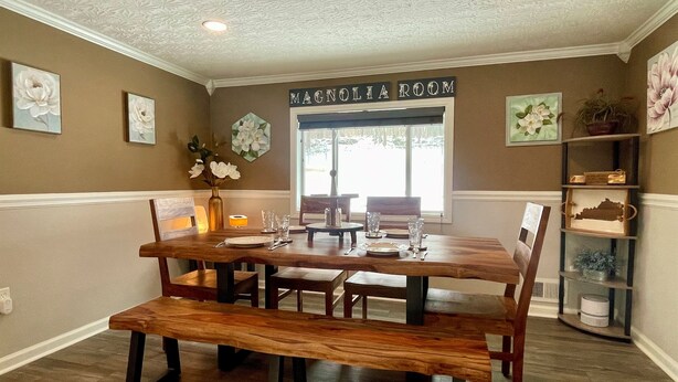 A dining room with a wooden table and benches, a window with a view, and a sign reading "MAGNOLIA ROOM".