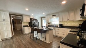 A modern kitchen with white cabinetry, a central island with bar stools, a refrigerator, and a coffee maker.
