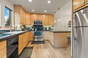 A modern kitchen with wooden cabinets, stainless steel appliances, and a black countertop.