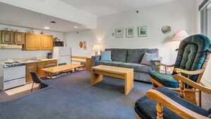 Een knus woongedeelte met een kitchenette, een bank, een houten salontafel en een schommelstoel.