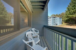 A balcony with a railing, a window, and two white plastic chairs.