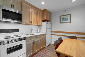Una cocina con armarios de madera, estufa, refrigerador y una mesa de comedor.