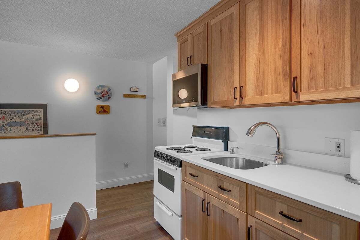 A kitchen with wooden cabinets, a white countertop, a stainless steel sink, and a stove.