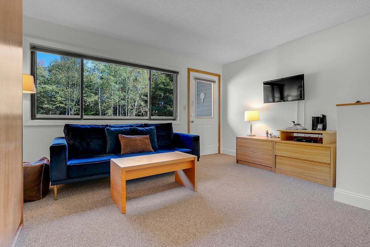 A room with a blue sofa, a wooden coffee table, a TV, and a desk with drawers.