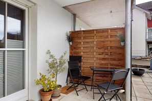 A patio area with a wooden wall, two chairs, a table, and potted plants. - Apartment 'Ketterer' with Terrace, Garden and Wi-Fi (Hüfingen)