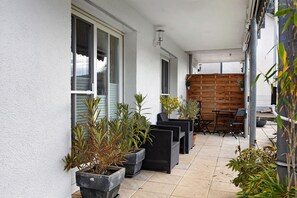 A covered outdoor patio with potted plants, wicker furniture, and a wooden wall. - Apartment 'Ketterer' with Terrace, Garden and Wi-Fi (Hüfingen)