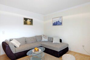 A modern living room with a grey sectional sofa, a glass coffee table with fruit, and two framed pictures on the wall. - Apartment 'Ketterer' with Terrace, Garden and Wi-Fi (Hüfingen)