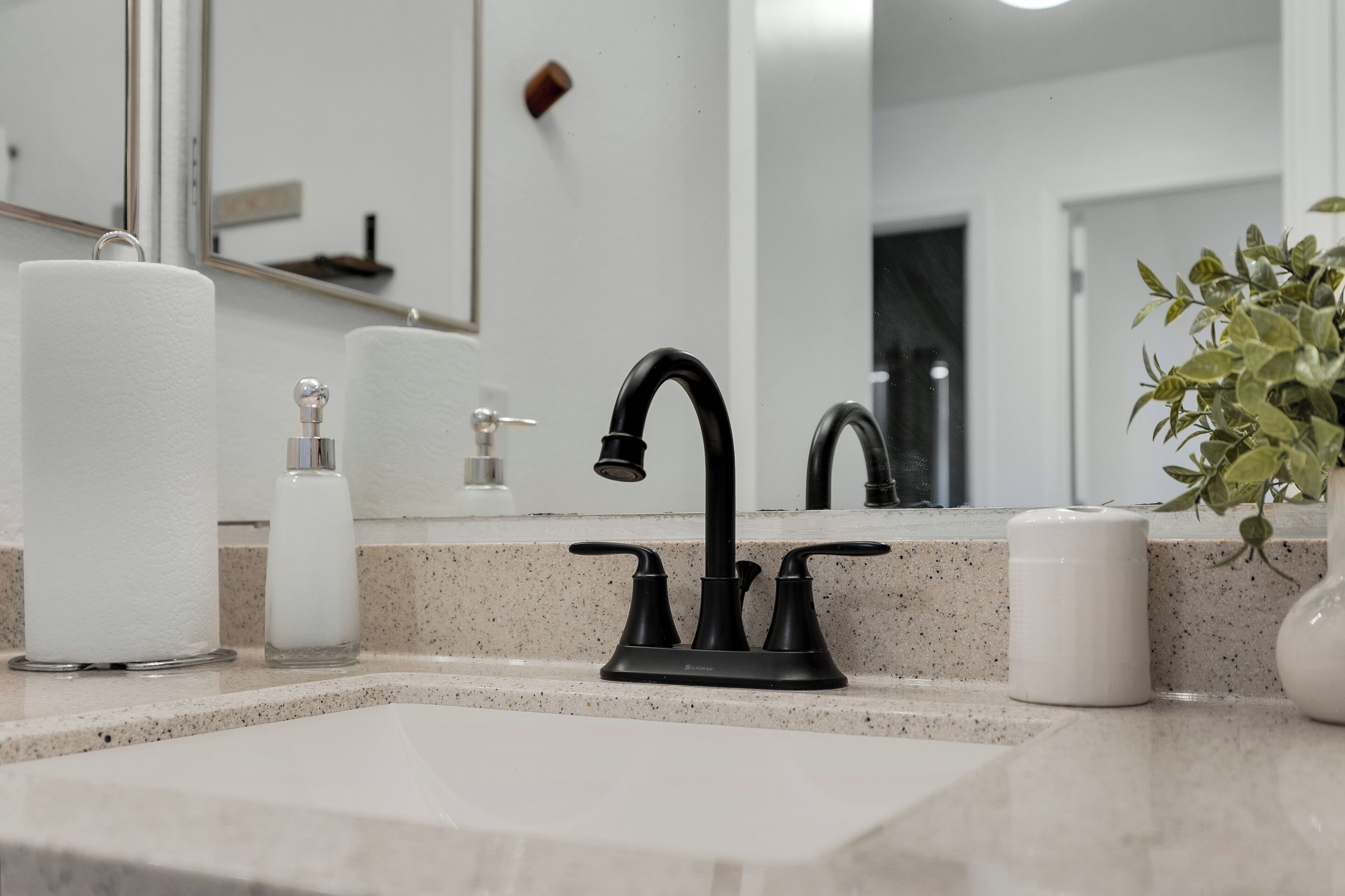 Une salle de bain avec un lavabo blanc, un robinet noir et un miroir au-dessus.