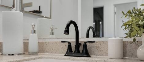 Une salle de bain avec un lavabo blanc, un robinet noir et un miroir au-dessus.