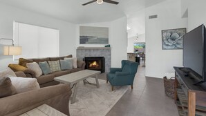 A living room with a sofa, armchair, coffee table, fireplace, TV, and artwork.