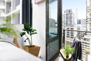 A modern apartment with a large window, a potted plant, a lamp, and a view of the cityscape. - A Lovely CBD Studio Right Next to Southern Cross (Melbourne)