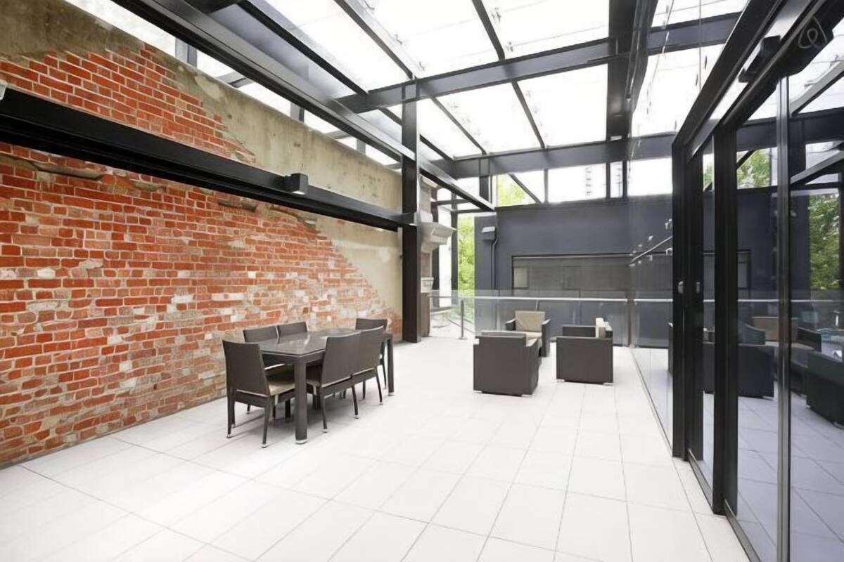 An outdoor patio with a brick wall, glass enclosure, and a grill area.