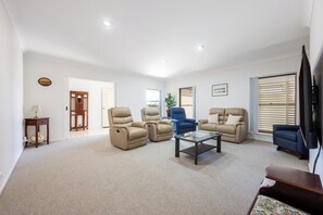 A spacious living room with beige sofas, a glass coffee table, and a television.