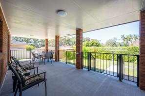 A covered outdoor area with two lounge chairs and a table, surrounded by a brick wall and a metal railing.